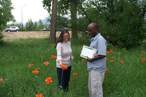 A man and woman outdoors in a place with grass and orange flowers with trees in the background.