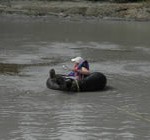 Woman floating in an inner tube on the surface of Upper Klawasi mud volcano in order to collect a sample.