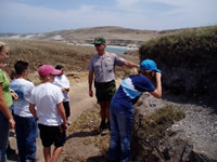 A man standing next to a rock outcropping explaining the geology to a group of kids.
