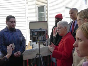 Former EPA Administrator Gina McCarthy in a red suit demonstrating an air sensor to community members in Newark, New Jersey.