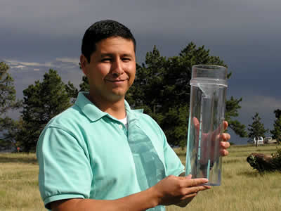 A man outside holding a large rain gauge.