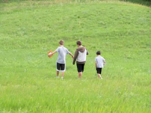 Three kids walking through a field of grass.