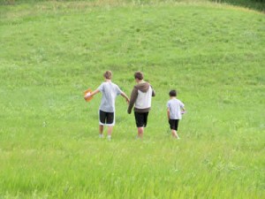 Three kids walking through a field of grass.