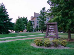 Sign in large lawn with institutional building in back.