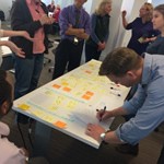 A group of people standing around a table with many sticky notes they've written on and attached to the table.