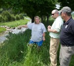 Two men and a woman standing next to a stream talking.