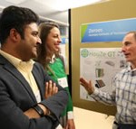 Man talking to a man and woman in front of a display on a bulletin board.