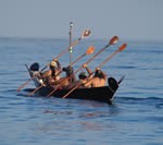 A group of men in native attire in a native boat on the water.