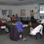 People around a table and one standing next to a presentation on screen in a workshop.