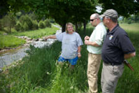 Two men and a woman standing next to a stream talking.