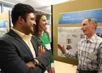 Man talking to a man and woman in front of a display on a bulletin board.