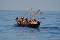 A group of men in native attire in a native boat on the water.