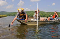 Man leaning over front of a boat in the water with an instrument to collect data.