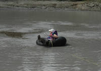Woman floating in an inner tube on the surface of Upper Klawasi mud volcano in order to collect a sample.