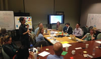 In a collaboration space with projectors and whiteboards, a group of employees listen to a speaker’s speech.